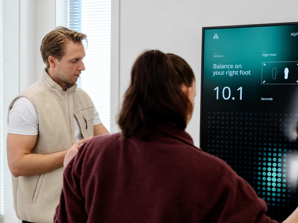 A trainer and member beside the Alphatek display showing a balance activity.