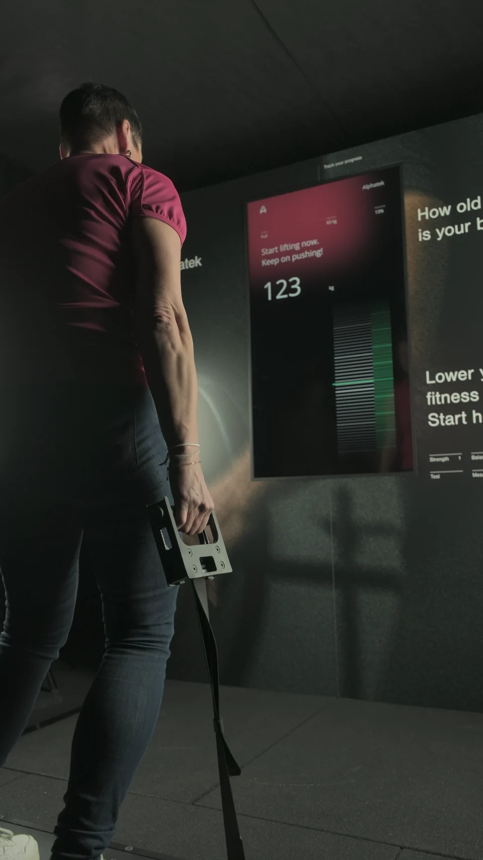 A participant pulls the handles while the Fitness Age display shows the strength measurement.