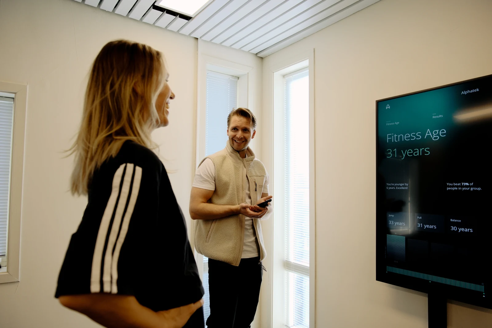 A member and trainer talk beside the Alphatek display showing a Fitness Age result.