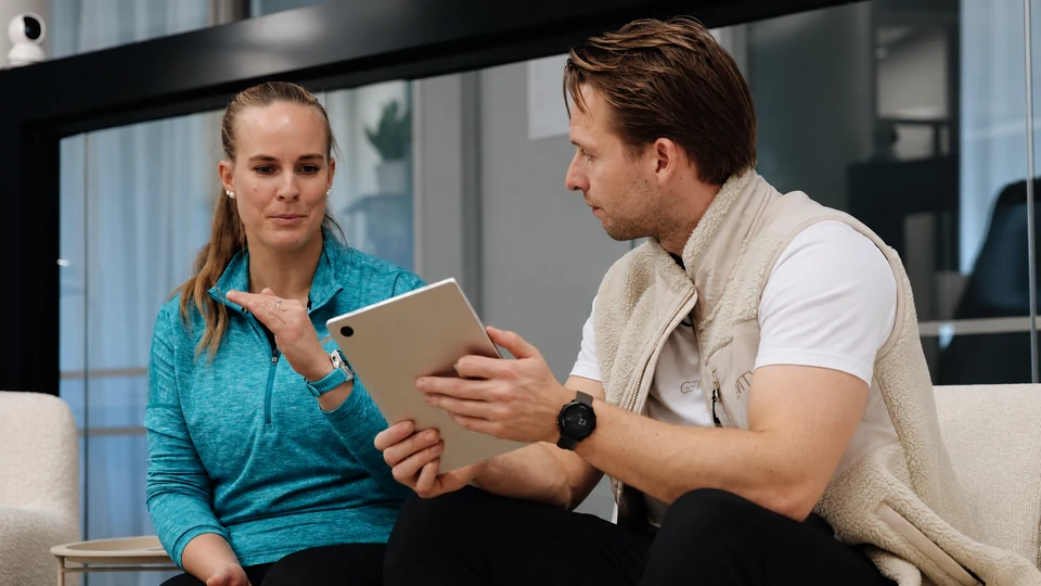 A member and trainer review a tablet and discuss it together.