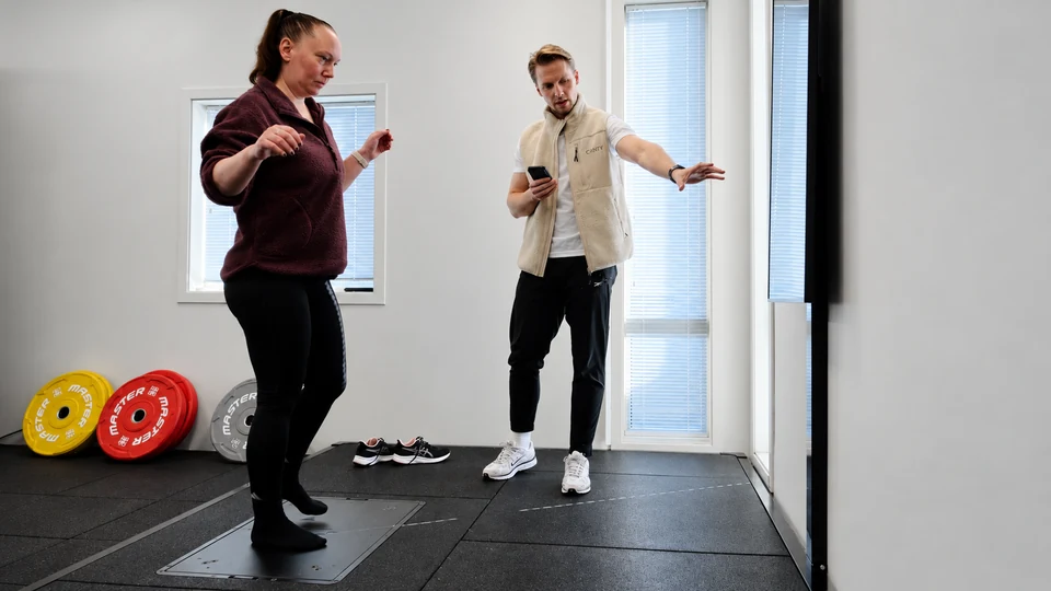 A member performs a balance activity on the Alphatek platform with guidance from a trainer.