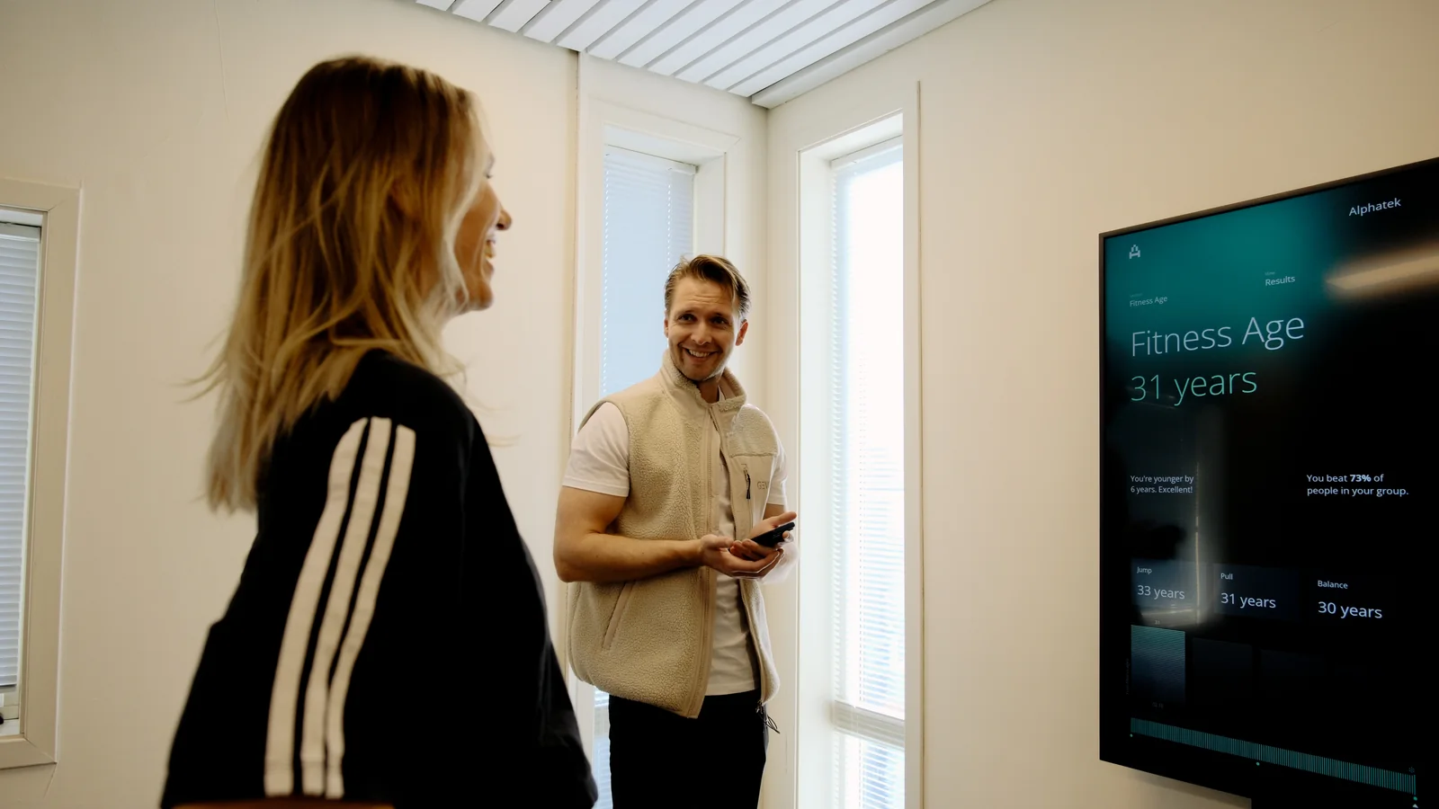 Two people discuss a Fitness Age result beside the Alphatek display.